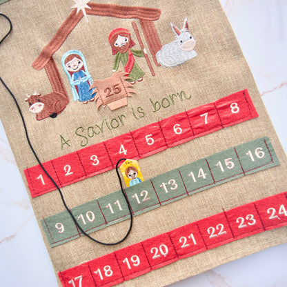 Close-up of embroidered Nativity scene and “A Savior is Born” design on a burlap-style fabric Advent calendar